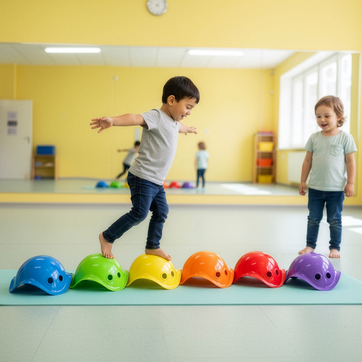A young boy balances on colorful Bilibo mini shells used as stepping stones on a blue mat in a bright playroom setting.