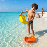 A young boy plays with colorful sand toys in the shallow water of a tropical beach in the Maldives.