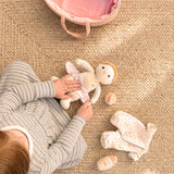 A child's hands changing a Dinky Dinkum doll on a woven rug next to doll clothes and a pink bag.
