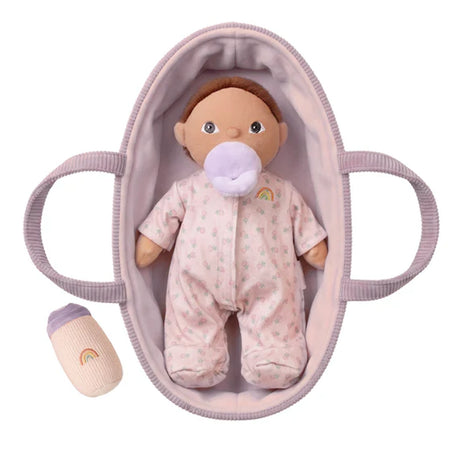 Olli Ella Dinkum Doll Pip in a pink floral onesie lying in a mauve bassinet with a pacifier and bottle.