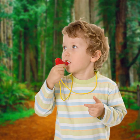 A young child with curly hair, wearing a striped shirt, stands in a forest, blowing a red whistle. The background is lush with green trees.