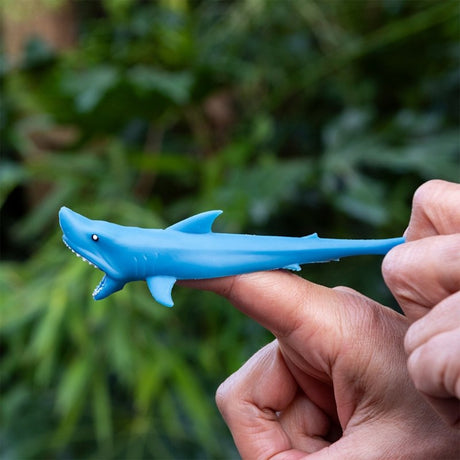 Blue stretchy rubber shark toy being pulled back on a finger like a catapult launcher.