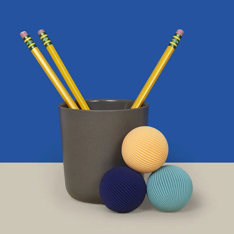 Three ridged Speks Odds fidget magnets on a desk next to a pencil holder with yellow pencils.