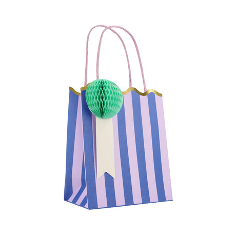 Blue and purple striped gift bag with a green honeycomb rosette, scalloped gold trim, and pink handles.