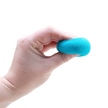A person squeezing a small, bright blue fuzzy toy ball between their fingers against a white background.