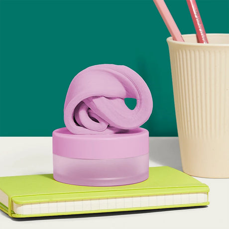Pink focus putty on its container, sitting on a lime-green notebook next to a cup with pencils.