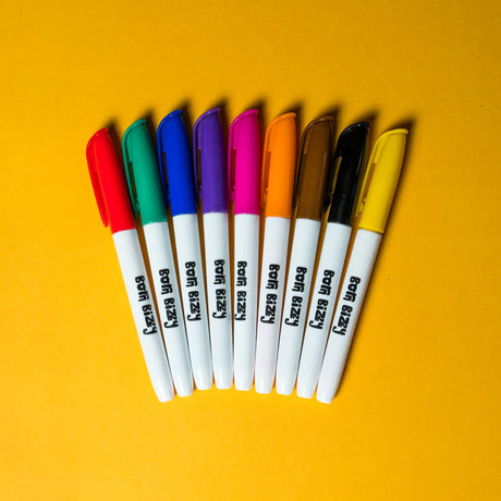 Nine colorful marker pens with white barrels branded "Born Bizzy" arranged in a fan shape on a yellow background.