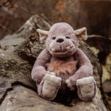 A soft grey plush monster toy seated on a wooden log in a natural outdoor setting.