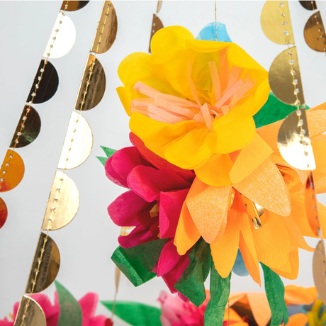 Close-up of bright yellow, orange, and magenta crepe paper flowers on a chandelier with gold foil trim.