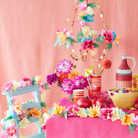 A vibrant paper floral chandelier suspended above a festive party table with colorful flowers and pink backdrop.