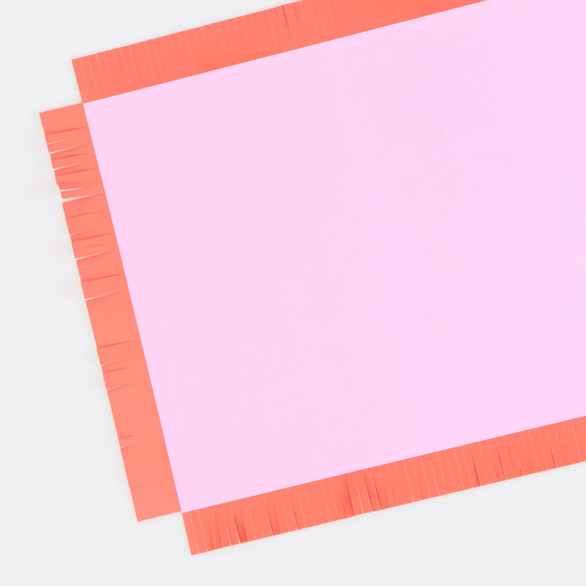Single pink paper placemat with an orange fringed border on a white background.