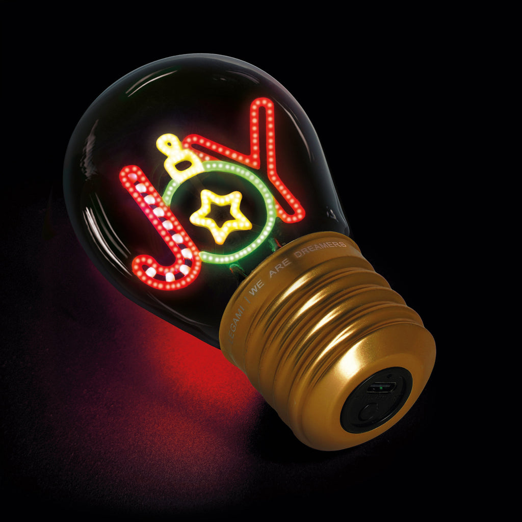 A glowing light bulb features the word "Joy" in festive red and green neon, decorated with a star and ornament. The base is gold, set against a dark background.