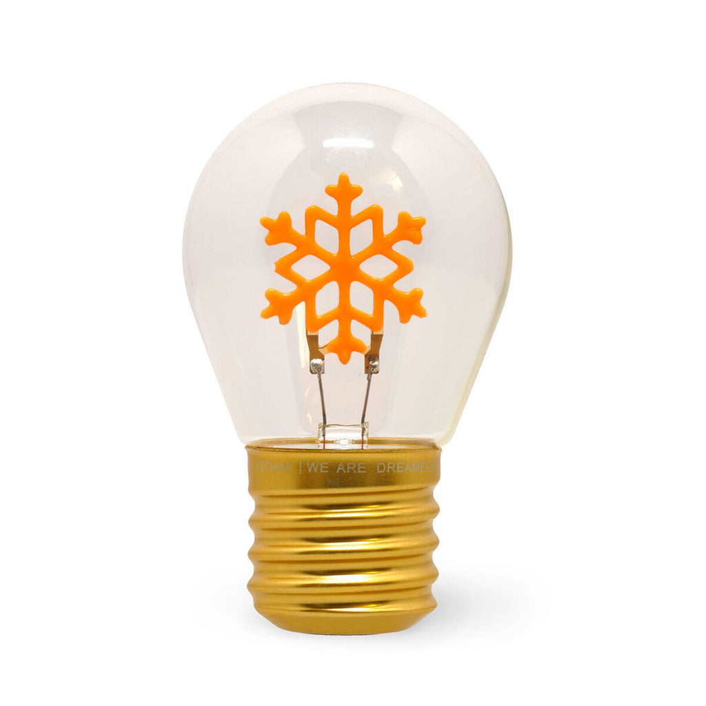 A clear glass light bulb with a golden base contains a bright orange snowflake design inside. The image conveys a creative, festive vibe.