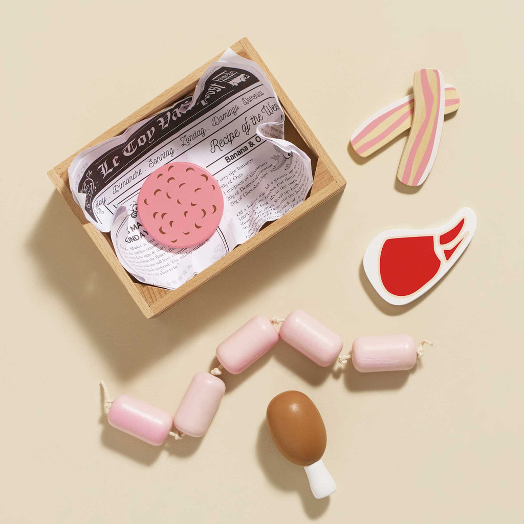 Wooden crate filled with toy food, including pink and white sausages, pizza slices, and drumsticks. Playful and colorful.