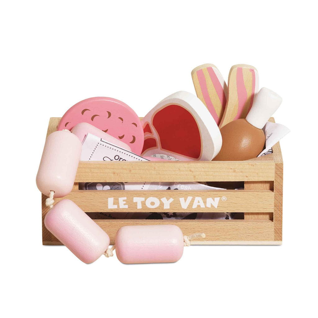 Wooden crate labeled "Le Toy Van" filled with toy food, including pink and white sausages, pizza slices, and drumsticks. Playful and colorful.