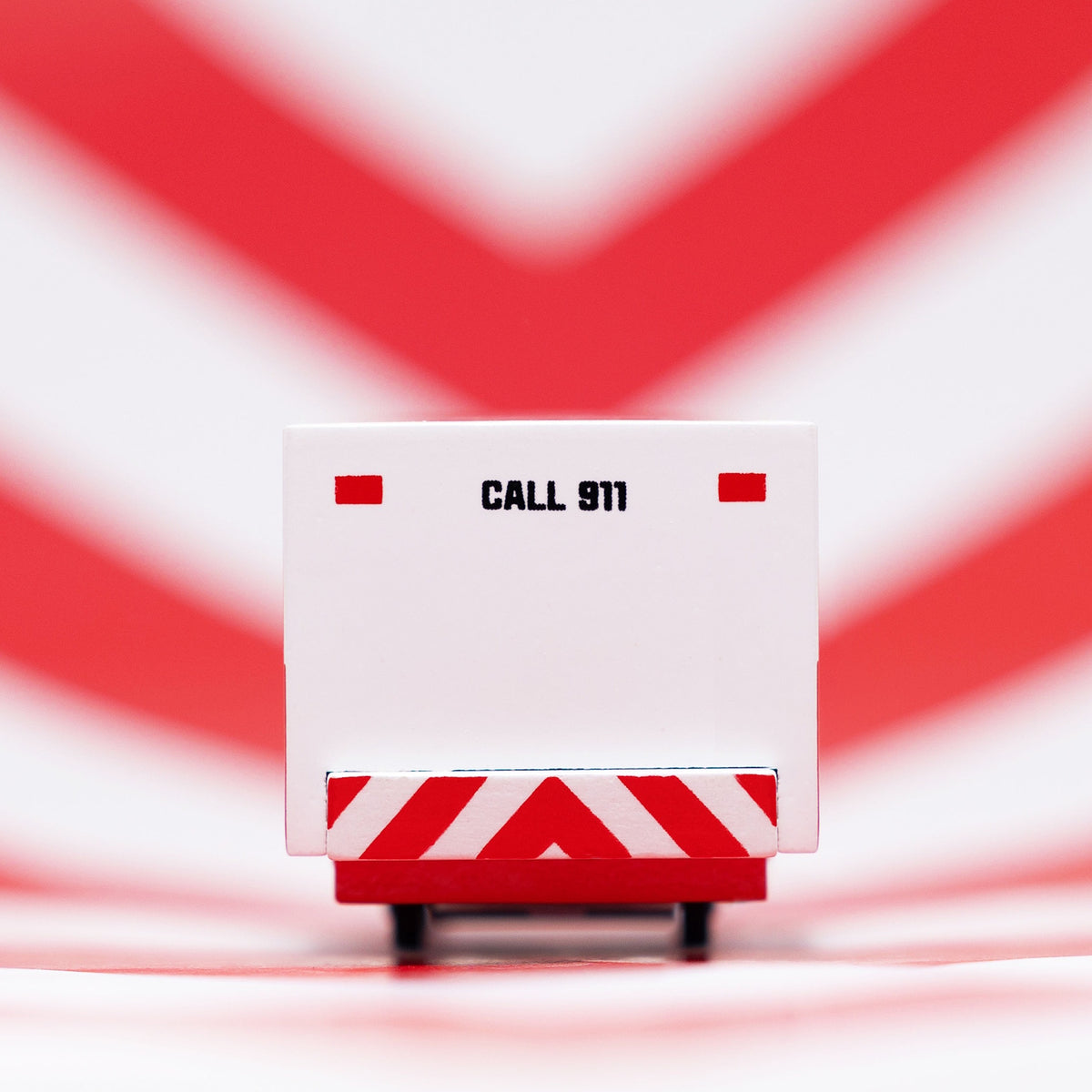 Rear view of a Candylab wooden ambulance toy car with "CALL 911" text, against a red and white chevron background.
