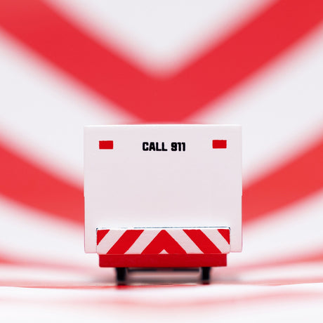 Rear view of a Candylab wooden ambulance toy car with "CALL 911" text, against a red and white chevron background.