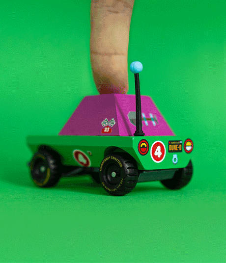 Small green and magenta toy adventure truck being pressed by a finger on a bright green background.