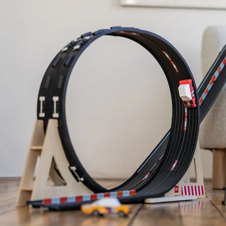 A small red and white toy car racing around a black circular loop track on a light wood floor.