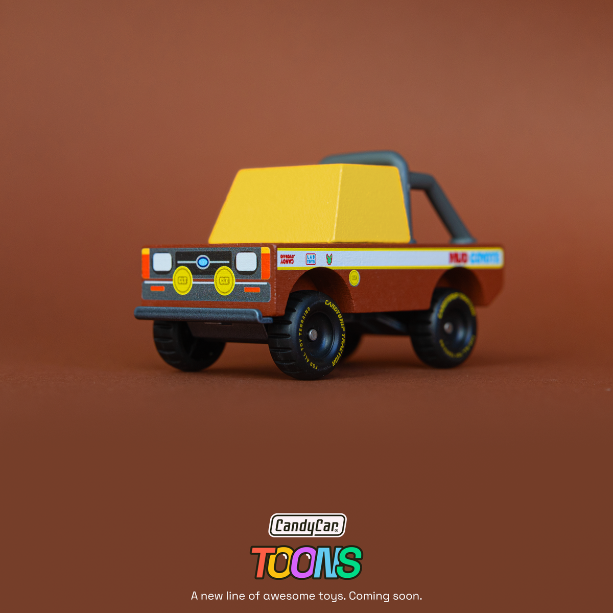 Small wooden toy off-road truck with yellow cab and "Mud Coyote" decals on a brown background. CandyCar Toons logo below.