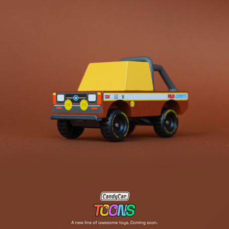 Small wooden toy off-road truck with yellow cab and "Mud Coyote" decals on a brown background. CandyCar Toons logo below.