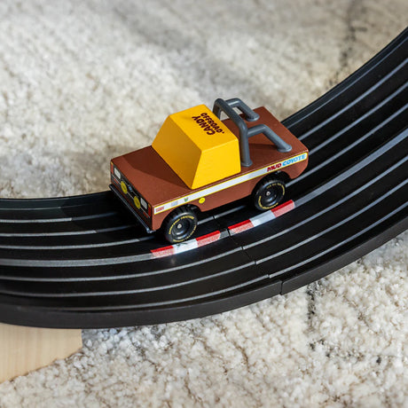 Wooden Candycar Mud Coyote toy truck racing on a black curved track over a white shag rug.