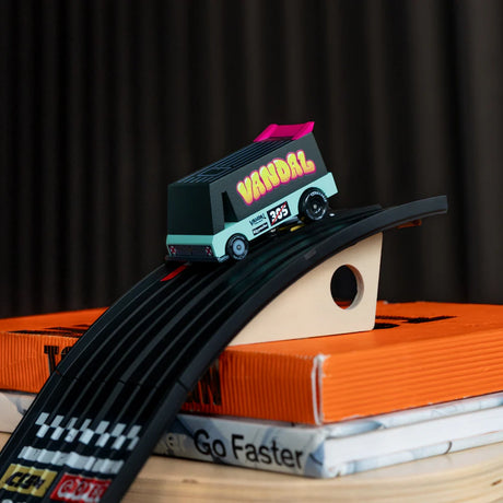 Candycar Toons Seafoam Vandal van toy on a black racing ramp, placed atop orange and white books in a lifestyle setting.