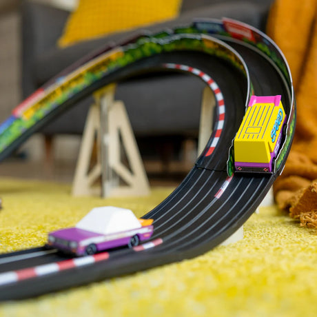Colorful wooden toy van and purple car racing on a banked track in a living room; Candycar Speed Vandal by Candylab.