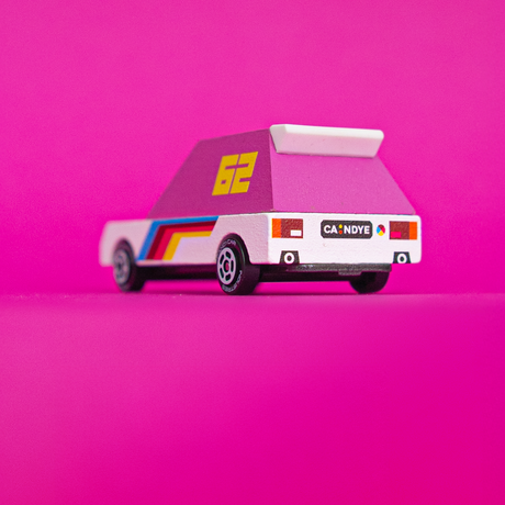 Retro-style wooden toy race car with pink top, number 62, and rainbow stripes on a vibrant pink background.