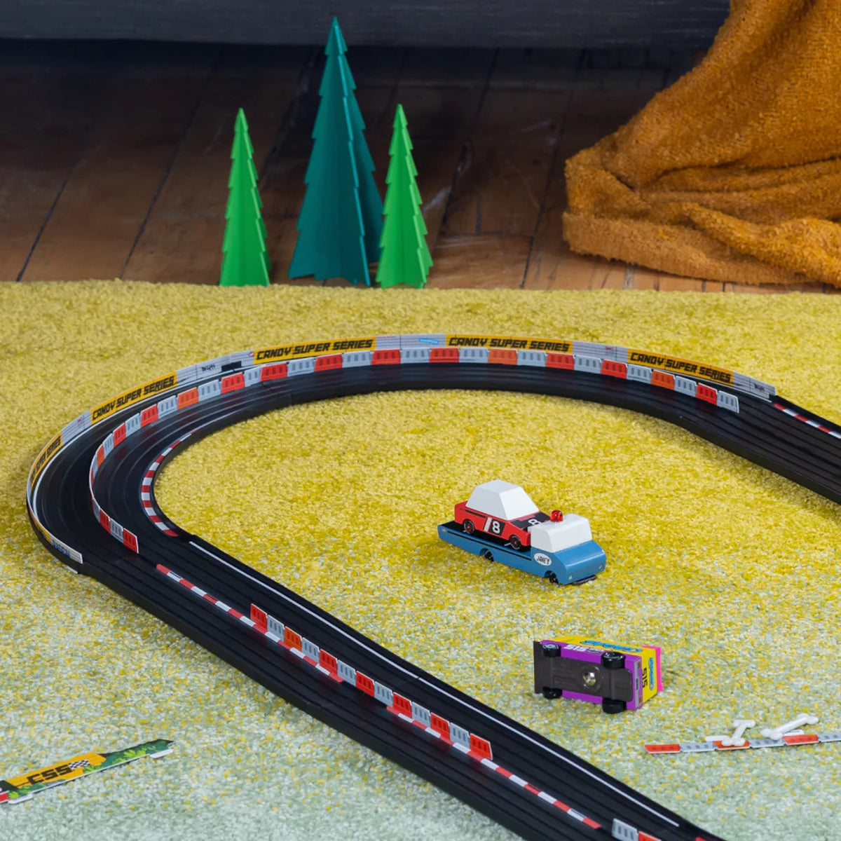 Candylab Roadworks toy race track expansion with wooden cars and 90-degree turn curves on a yellow rug.