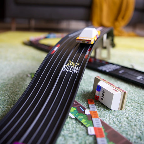 Toy wooden cars on a black flexible track with a bridge over a green rug, featuring "Don’t Slow" text and a police car.