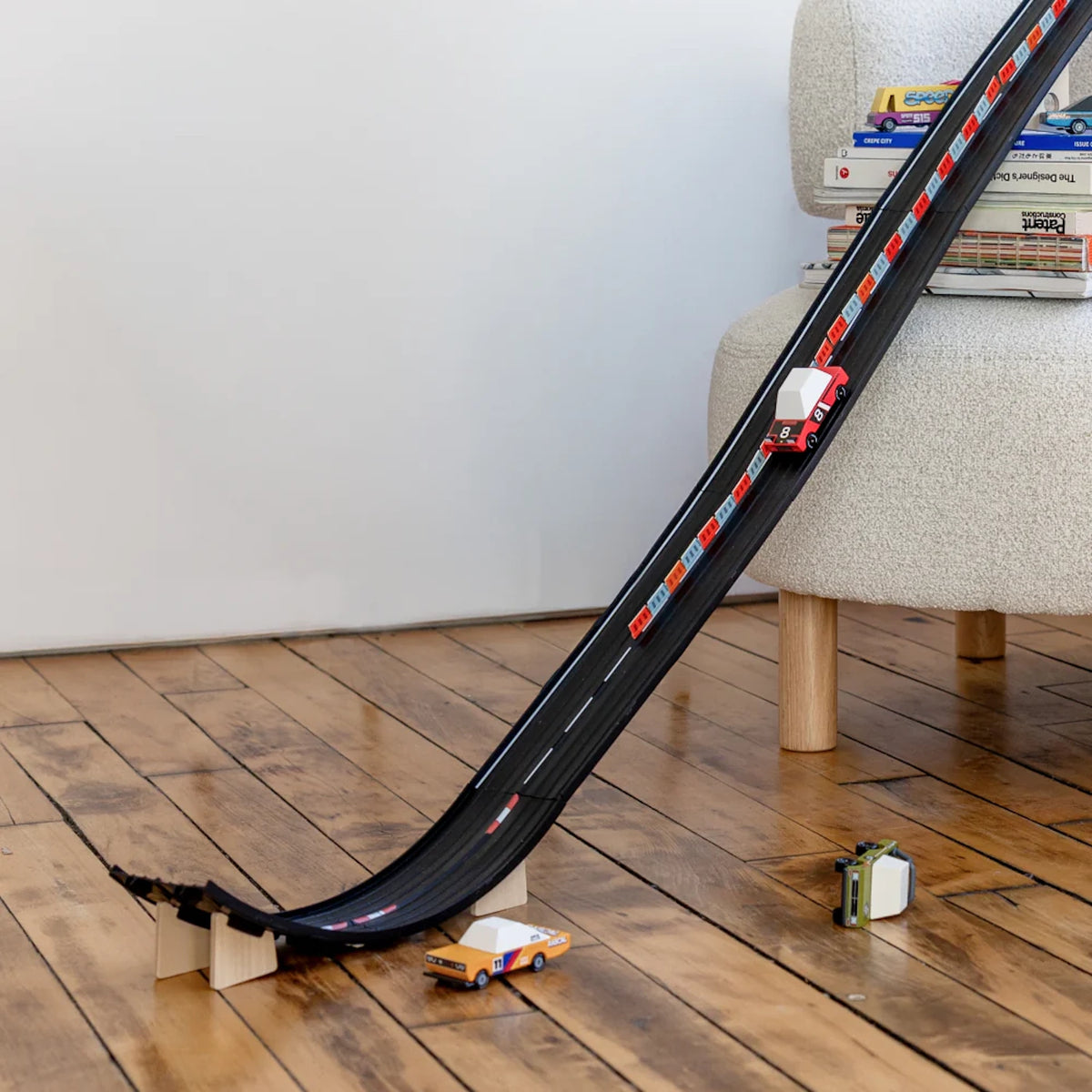 Candylab wooden toy cars racing down a long black rubber Roadworks track ramp on a hardwood floor.
