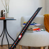 Candylab wooden toy cars racing down a long black Super Speed track leaning against a modern chair in a living room.