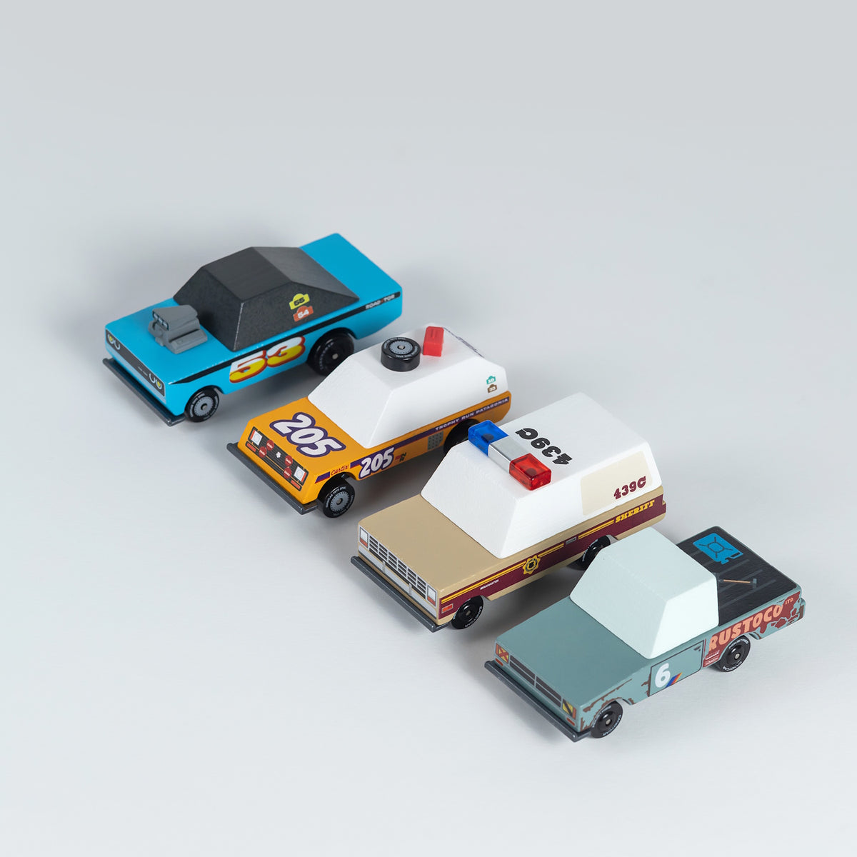 Four wooden Candylab toy cars, including a blue racer, yellow rally car, sheriff SUV, and teal pickup truck, in a row.