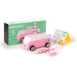 Pink wooden toy VW beach bus with its green packaging box, a toy surfboard, pop-top, and a sticker sheet.