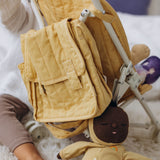 Honey-colored quilted diaper bag hanging on a doll stroller next to a plush baby doll.