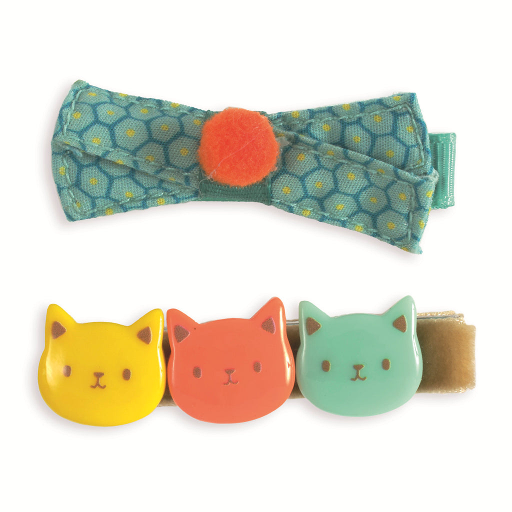 A teal fabric bow with yellow dots and an orange felt center sits above a clip with three cat faces in yellow, orange, and green, conveying a playful tone.