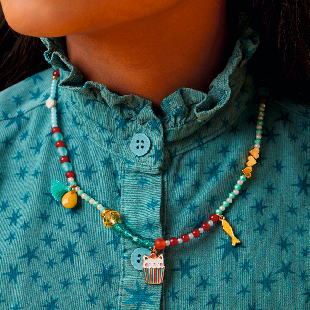 A child wearing a teal star-patterned shirt with a colorful beaded necklace featuring charms like a cat, fish, and hearts, conveying a playful tone.