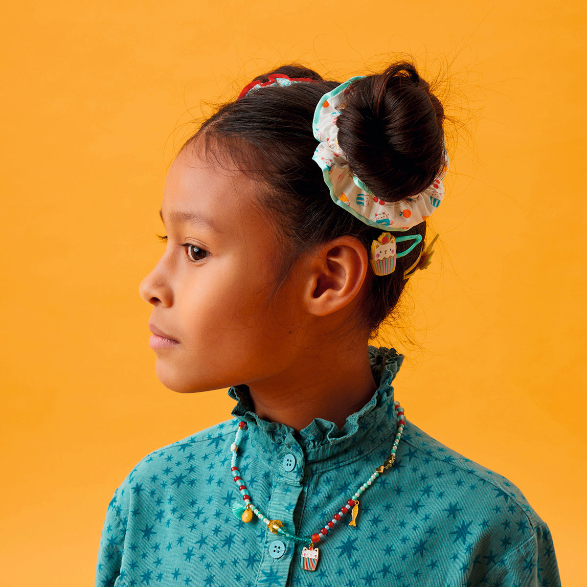 Girl wearing Mia cat collection beaded necklace with Emma scrunchie bun and cat cupcake hair clip accessories.