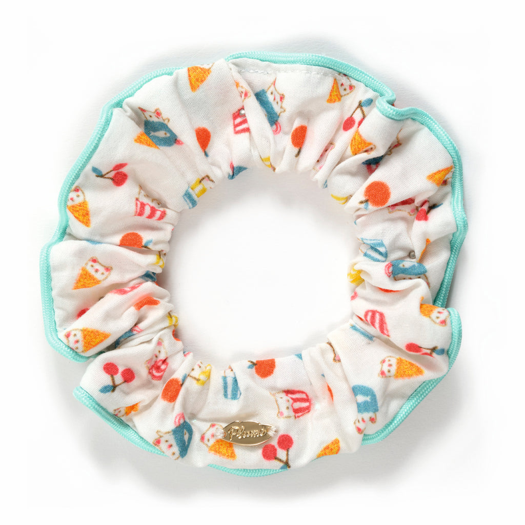 Cheerful scrunchie with ice cream cones and lollipops on white fabric, outlined in teal. Gold tag adds a playful, summery feel.