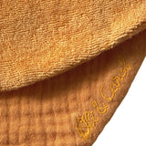 Close-up of orange muslin and terry cloth baby bib fabric with "Oli & Carol" embroidered in yellow thread.
