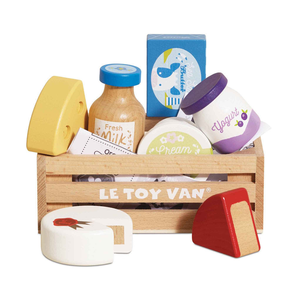 Wooden toy crate labeled "Le Toy Van" containing colorful toy groceries: milk bottle, cheese, yogurt, and cream. Bright, playful, and inviting.