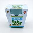 Packaging for a "Grow Your Own Cress" kit, showing a blue bamboo pot and cartoon smiling cress sprouts.