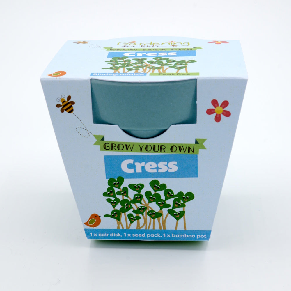 Packaging for a "Grow Your Own Cress" kit, showing a blue bamboo pot and cartoon smiling cress sprouts.