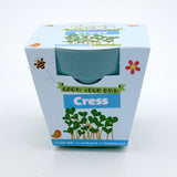 Packaging for a "Grow Your Own Cress" kit, showing a blue bamboo pot and cartoon smiling cress sprouts.