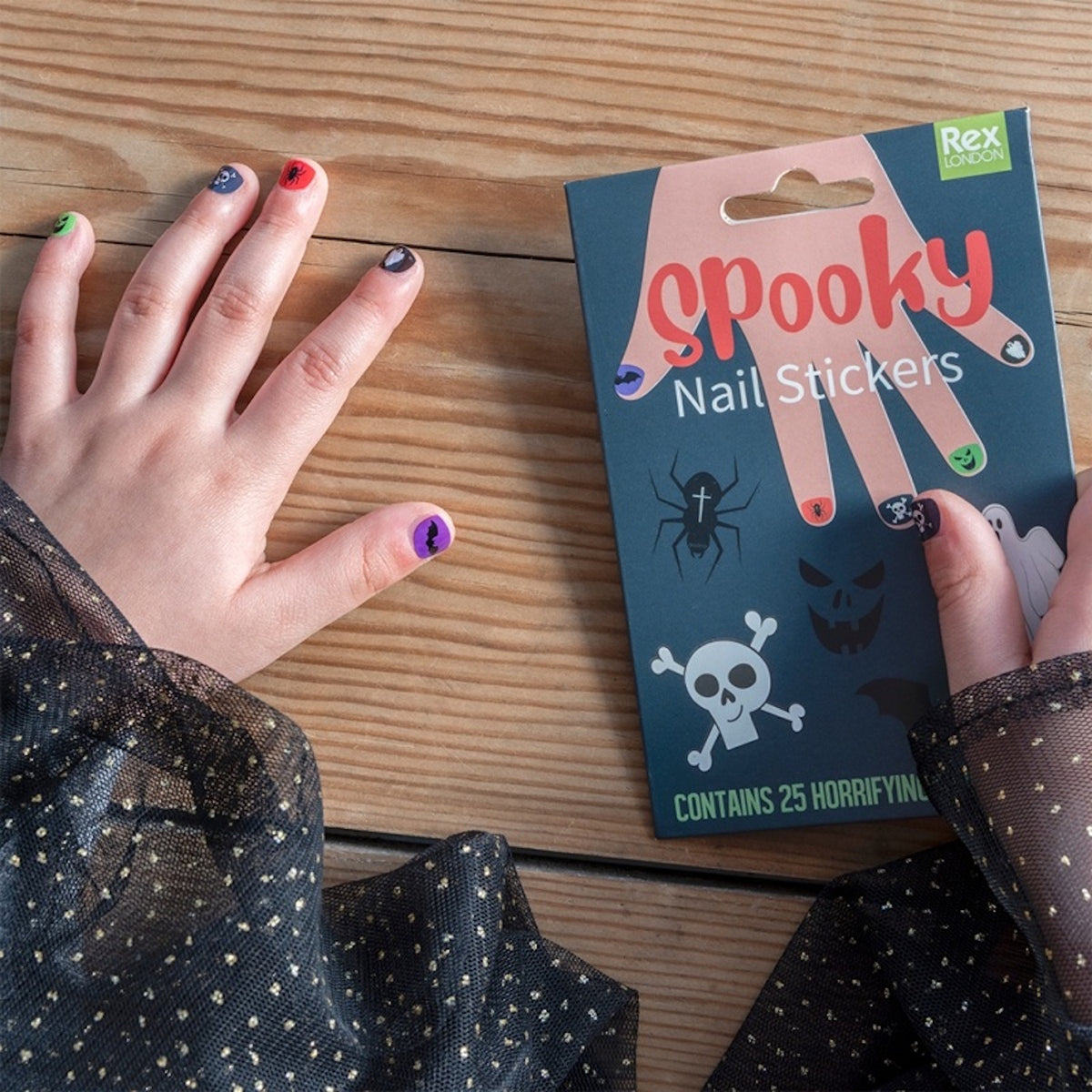 Child's hands showing applied spooky nail stickers next to the product package on a wooden table.