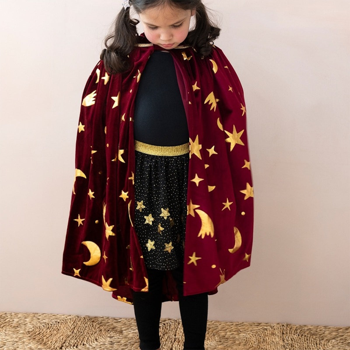 Young girl wearing a kids burgundy velvet wizard cape with metallic gold stars and crescent moons.