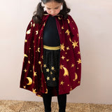 Young girl wearing a kids burgundy velvet wizard cape with metallic gold stars and crescent moons.