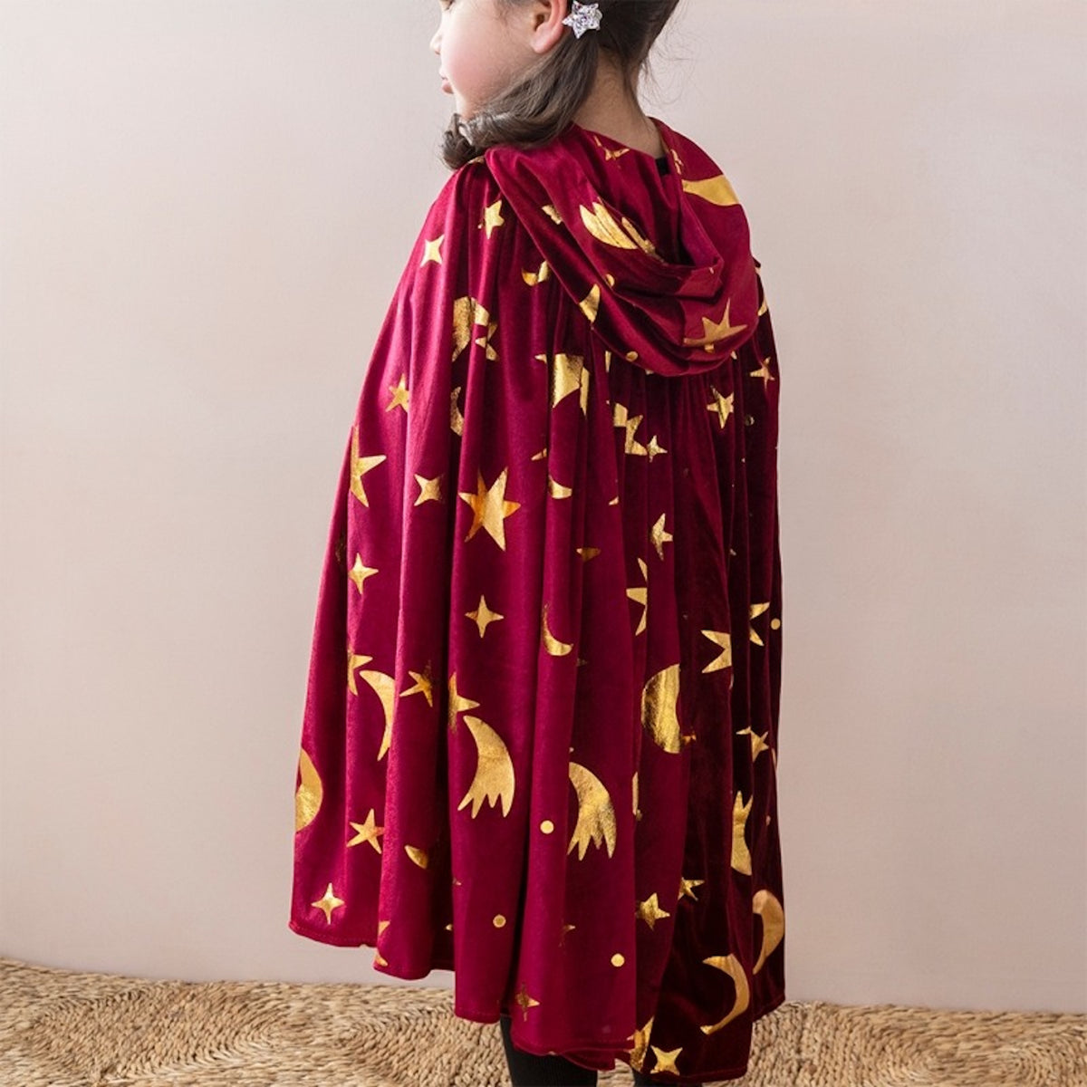 Child in a maroon and gold wizard cape with stars and moons, wearing a matching star hair clip.