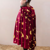 Child in a maroon and gold wizard cape with stars and moons, wearing a matching star hair clip.